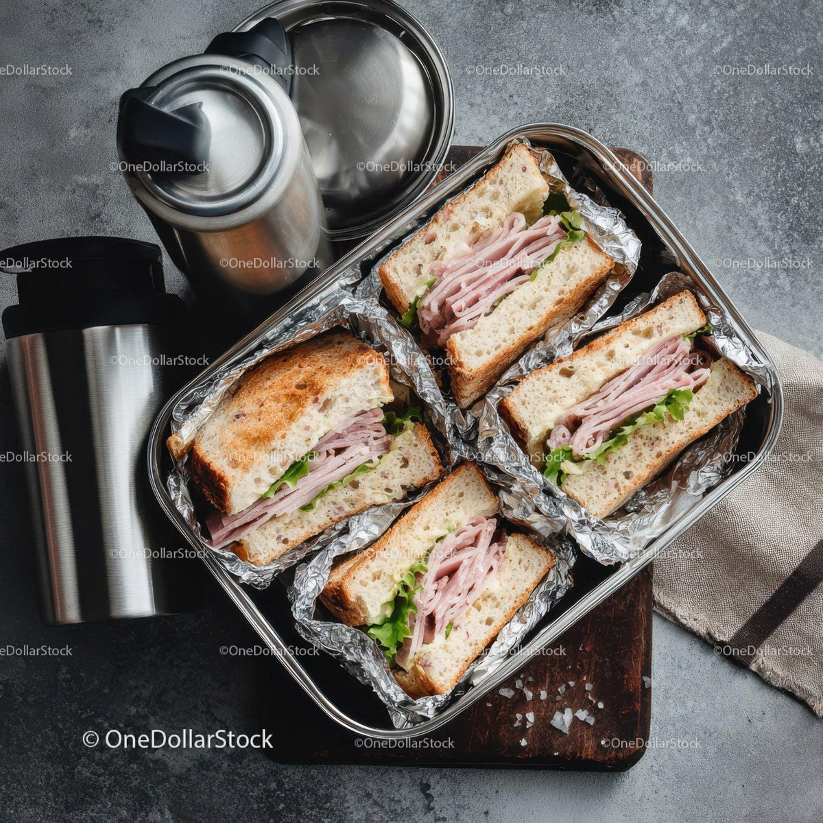 Ham and Lettuce Sandwiches in Aluminum Foil with Thermos on Brown Wooden Surface