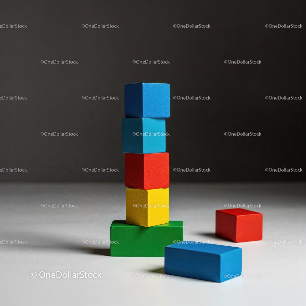 Stacked colorful wooden blocks with two loose blocks on white surface and dark background.
