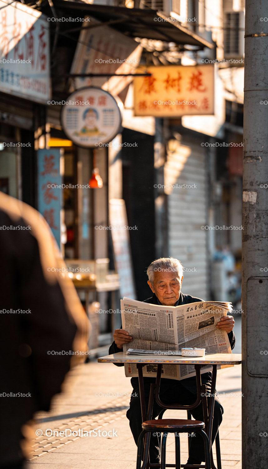 Elderly Man Reading Newspaper at Outdoor Street Cafe