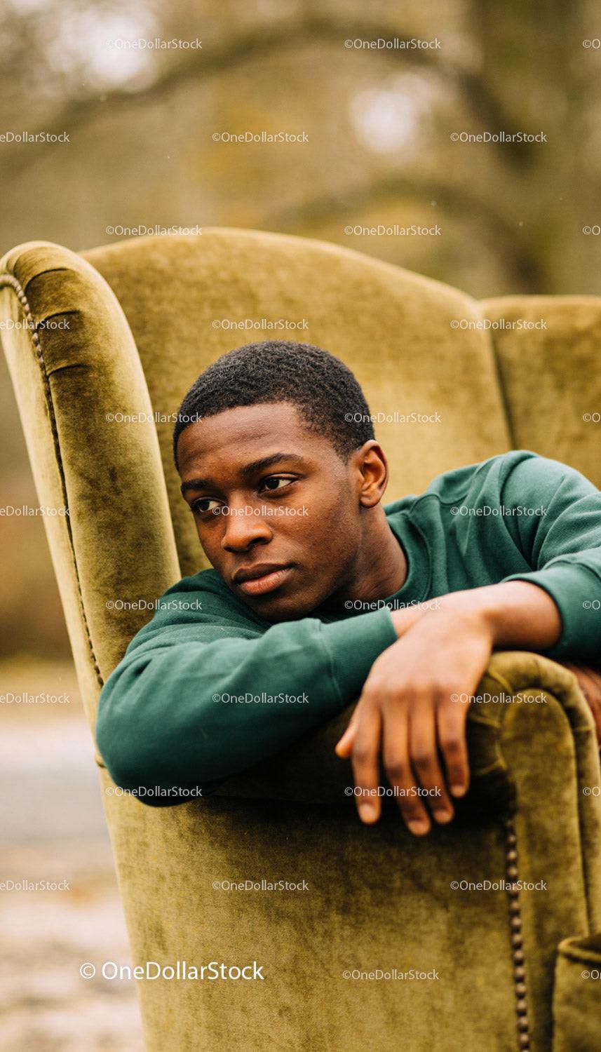 Thoughtful young man resting on vintage armchair outdoors