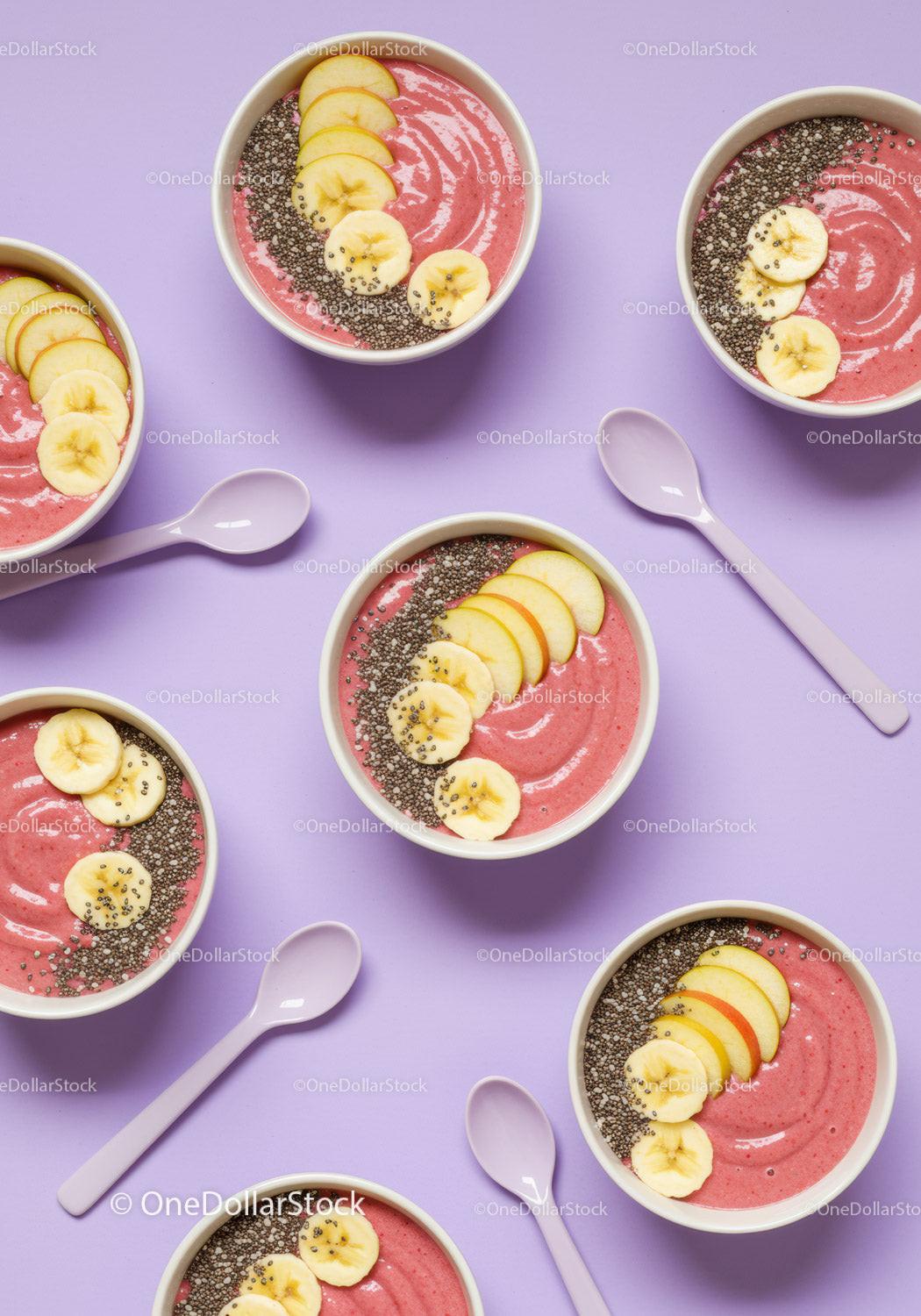Pink smoothie bowls with banana and apple slices on lilac