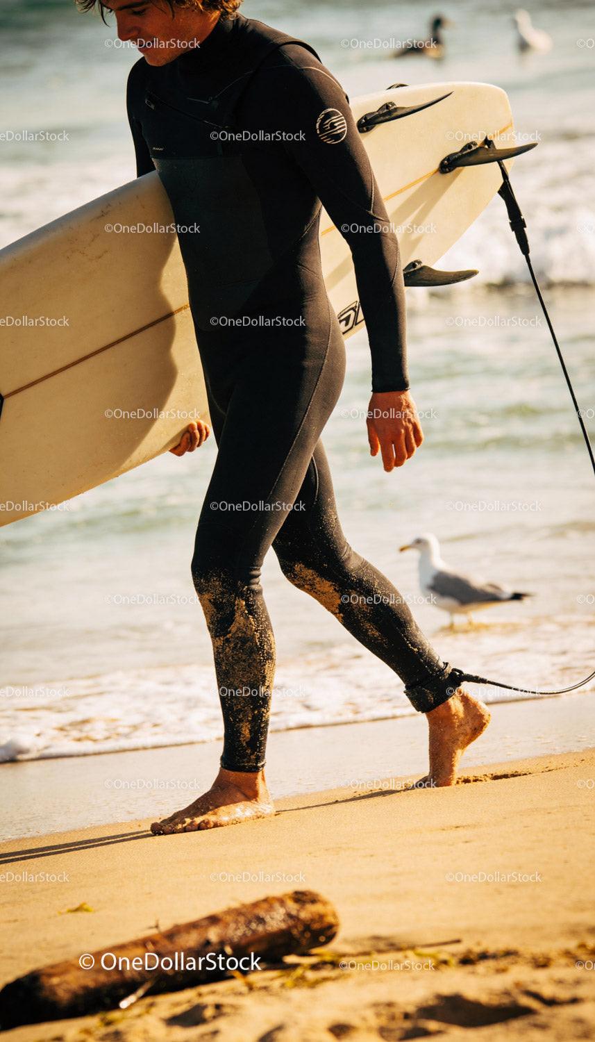 Surfer walking barefoot on sandy beach with surfboard