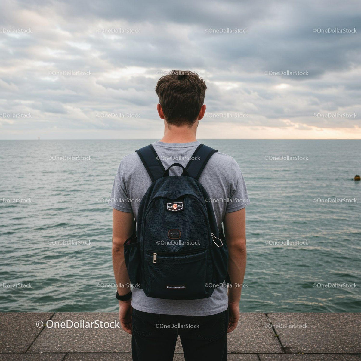 Young Man Standing by the Seaside with Backpack Enjoying Sunset