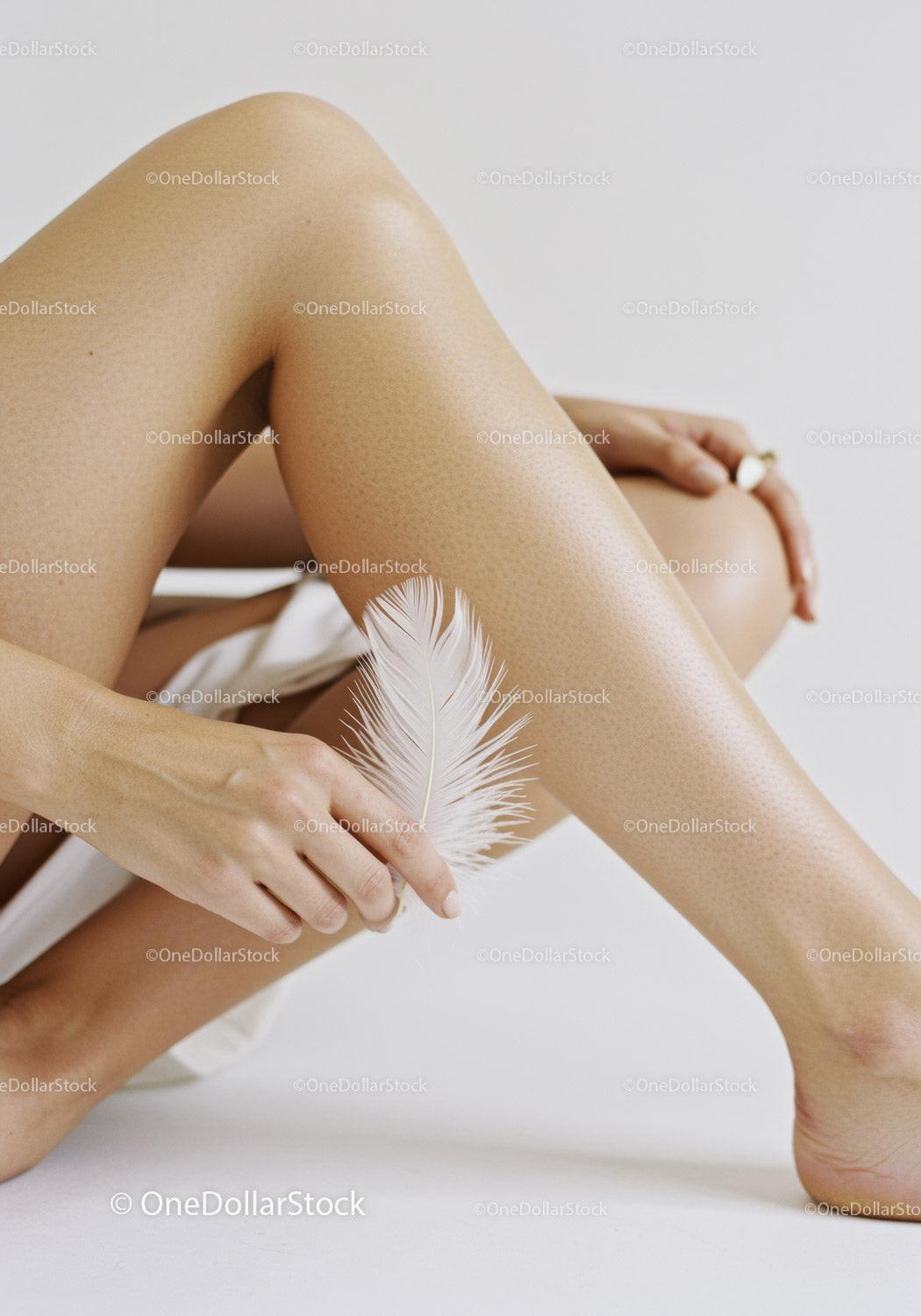 Close-Up of Tanned Legs with Sheer Nude Tights Holding Feather
