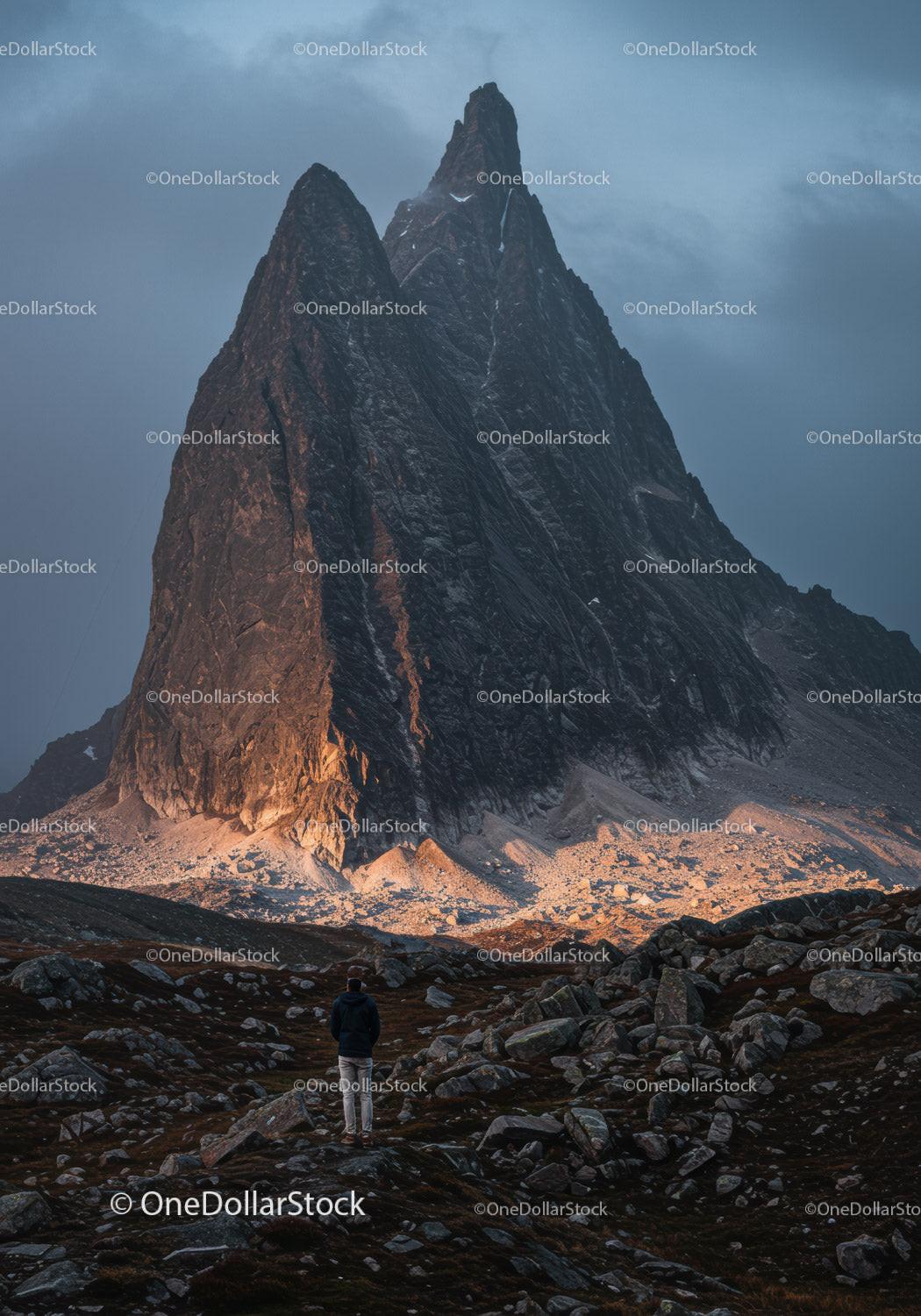 Solitary hiker facing towering mountain at dusk