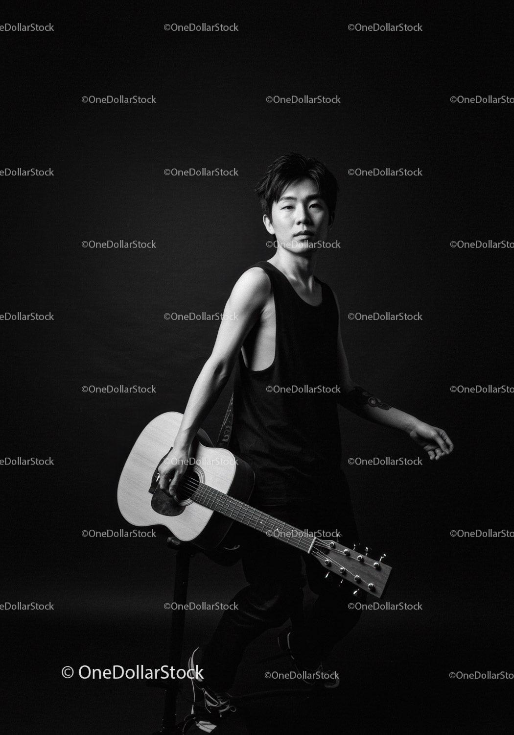 Young man holding acoustic guitar in dark studio