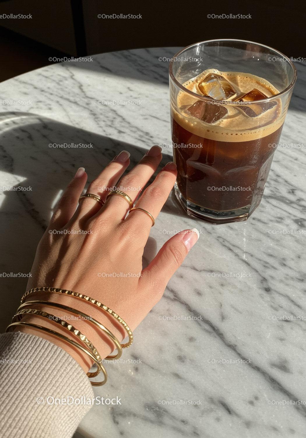 Hand with Gold Bracelets and Rings Next to Iced Coffee