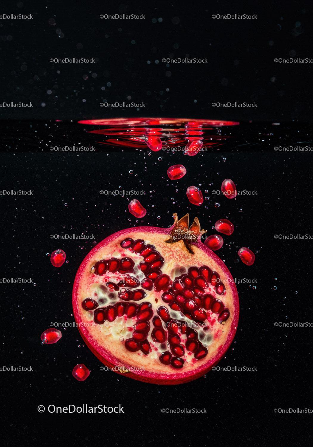 Fresh pomegranate halves with seeds falling underwater
