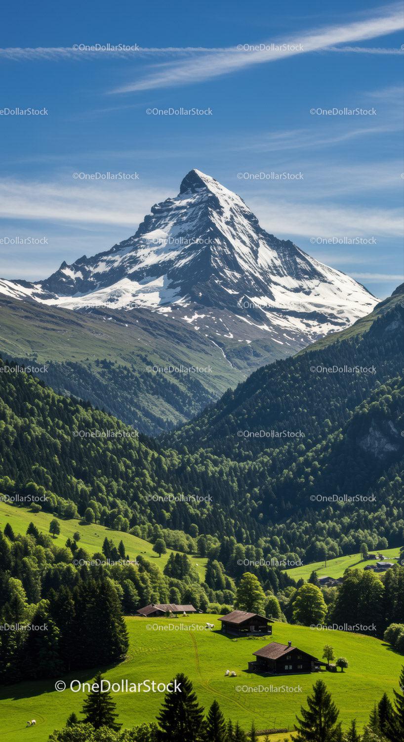 Snow-Capped Mountain Over Green Valley with Wooden Cabins and Blue Sky