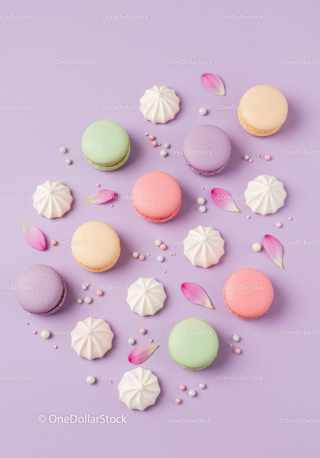 Colorful macarons and meringues with flower petals on purple