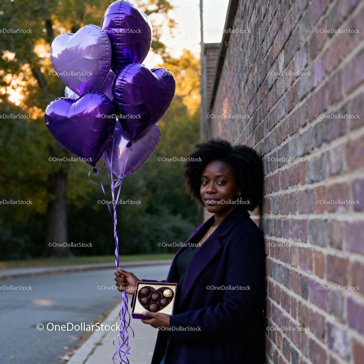 Woman holding heart balloons and chocolates by brick wall