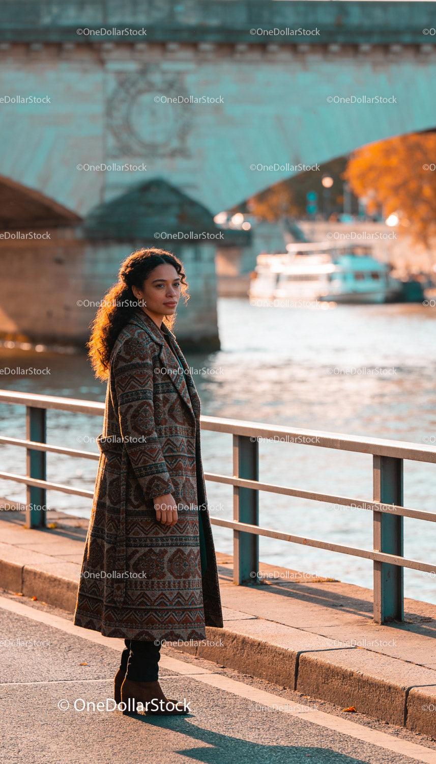 Woman in patterned coat standing by riverside in autumn