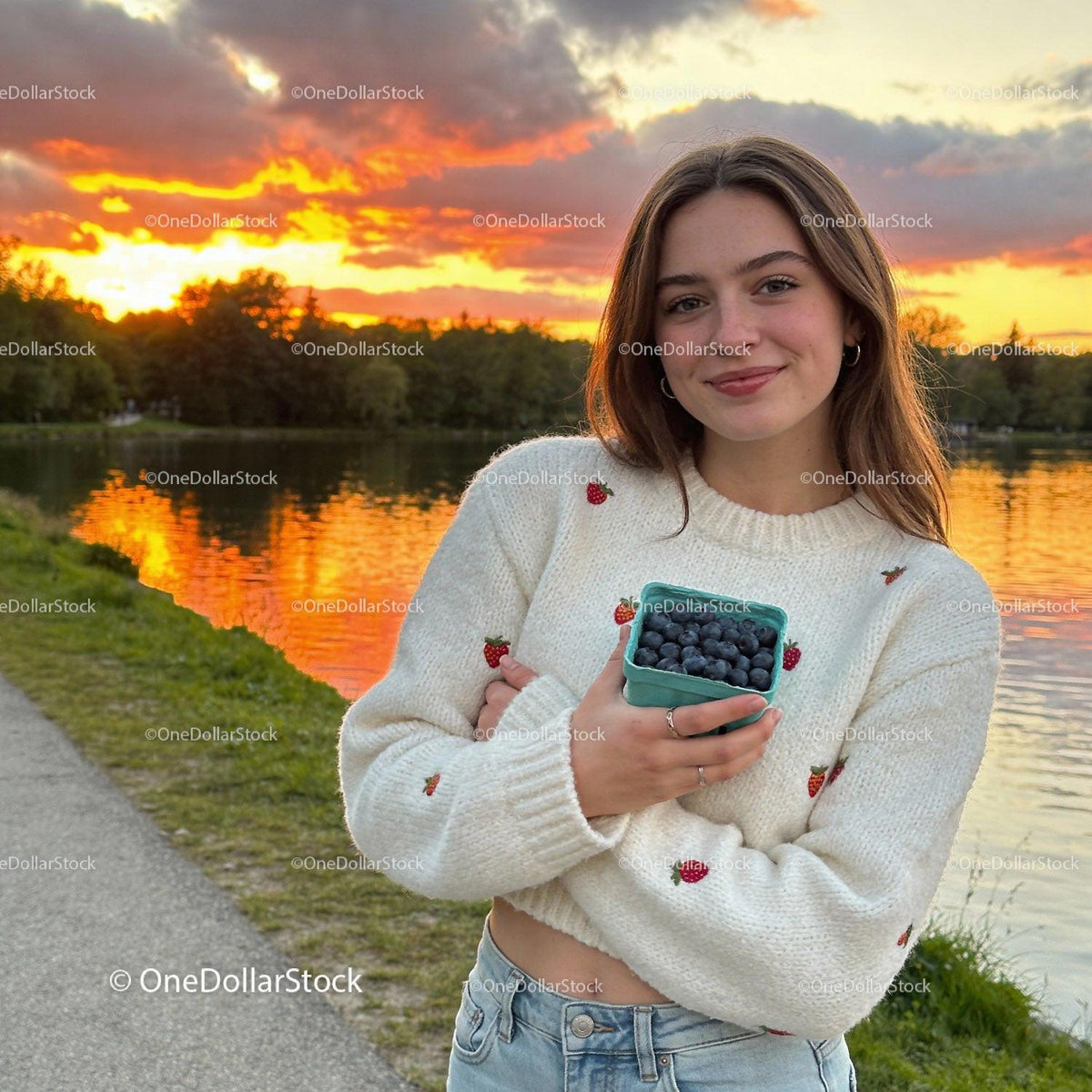 Young woman enjoying fresh blueberries by lake at sunset
