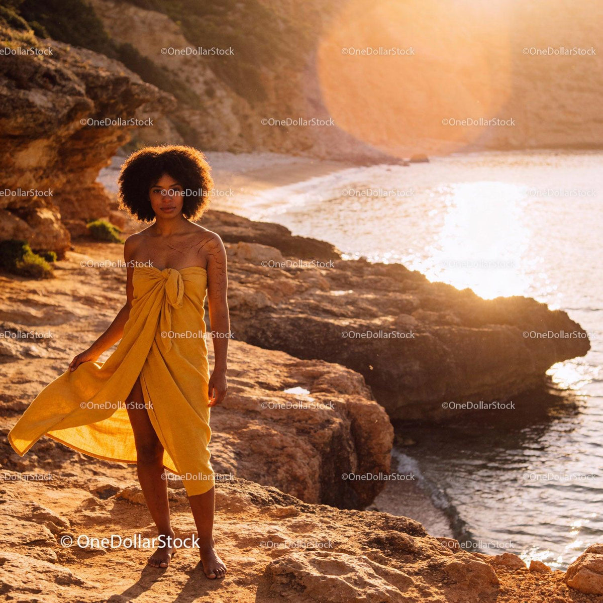 Woman in Yellow Wrap Standing on Rocky Beach at Sunset