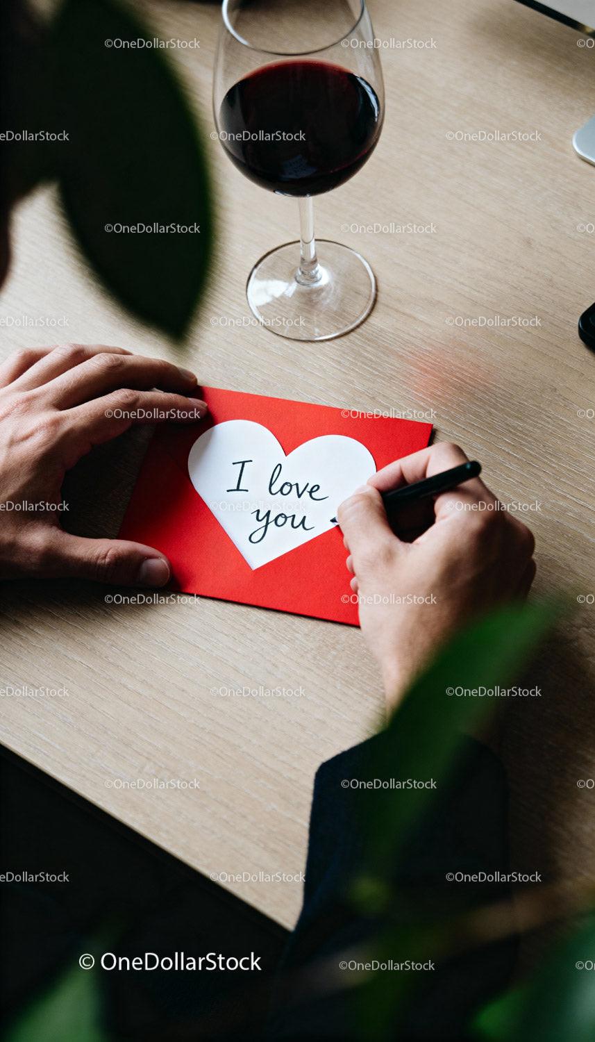 Writing a heartfelt love note next to a red wine glass
