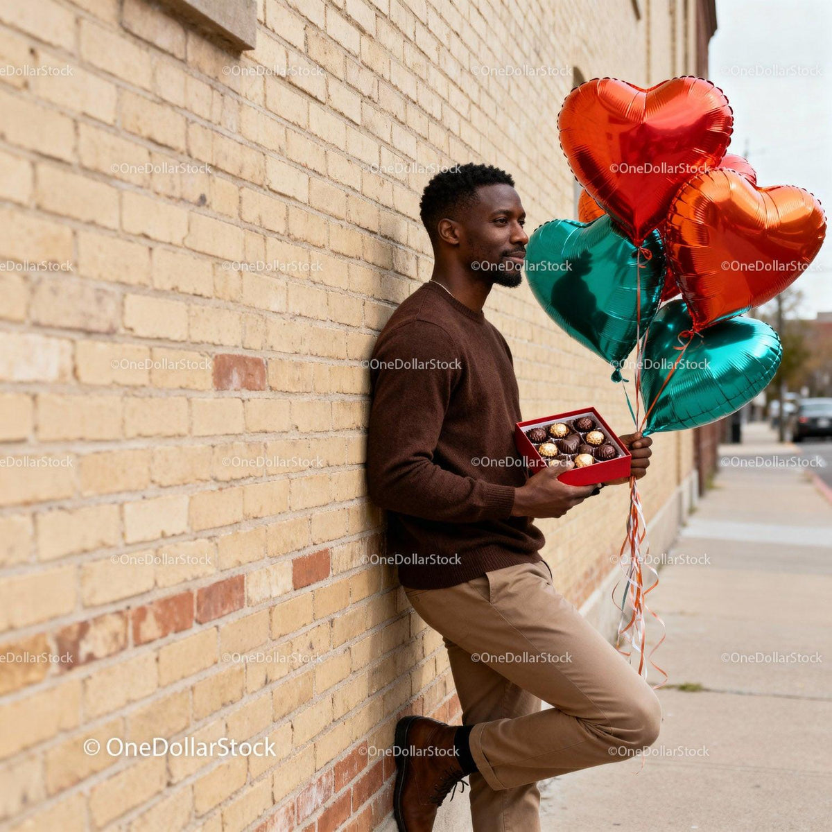 Man Holding Heart Balloons and Chocolates by Brick Wall