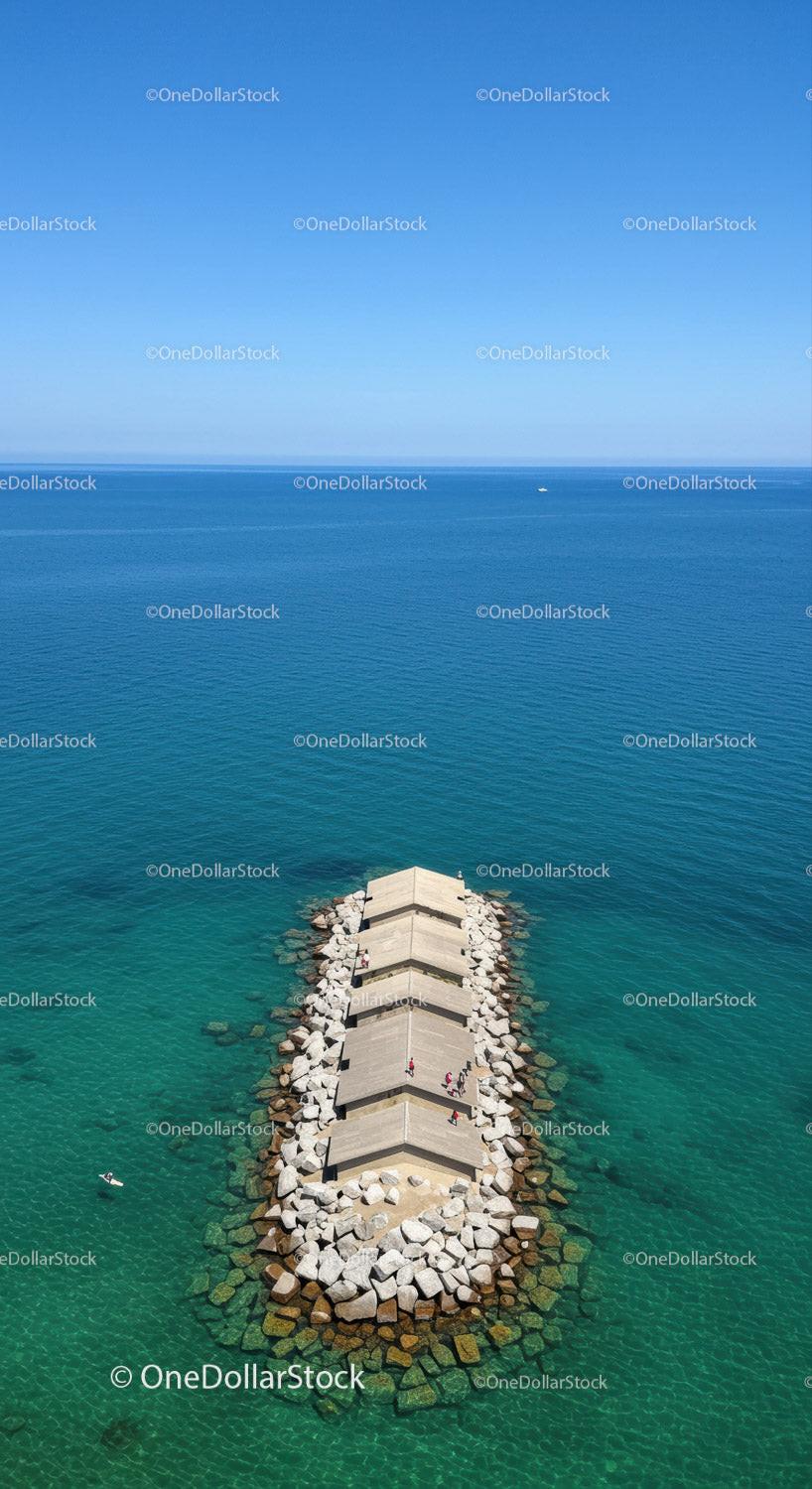 Serene Ocean Pier with Rocks Extending into Turquoise Waters and Clear Sky