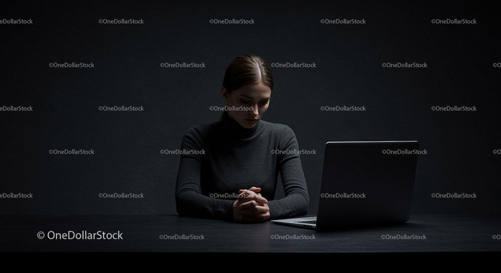 Contemplative Woman in Dark Workspace with Laptop