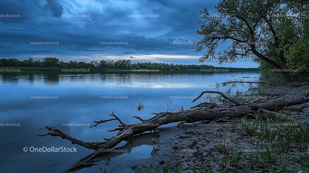 Tranquil Lake with Dramatic Sky and Fallen Tree at Dusk