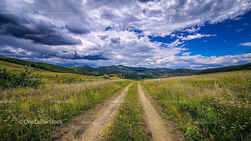 Dirt Road Leading Through the Rolling Hills Under Dramatic Skies