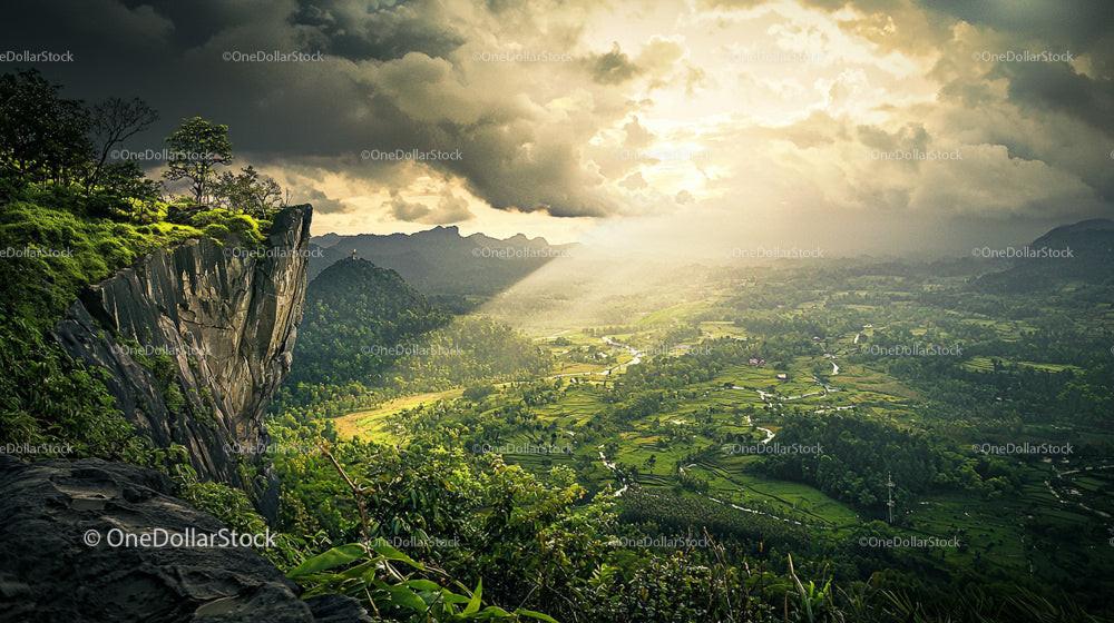 Sunlit Valley with Dramatic Clouds and Rocky Cliff