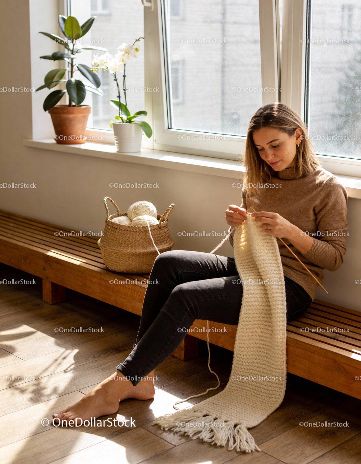 Woman knitting a cozy white scarf in a sunlit room