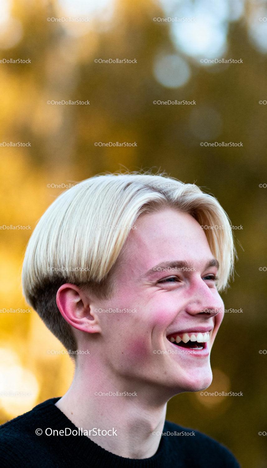 Young man with blonde hair laughing outdoors in soft light