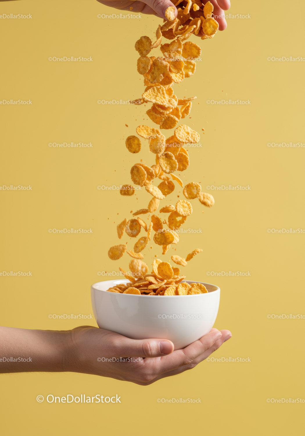 Hand Pouring Crunchy Cornflakes into White Bowl