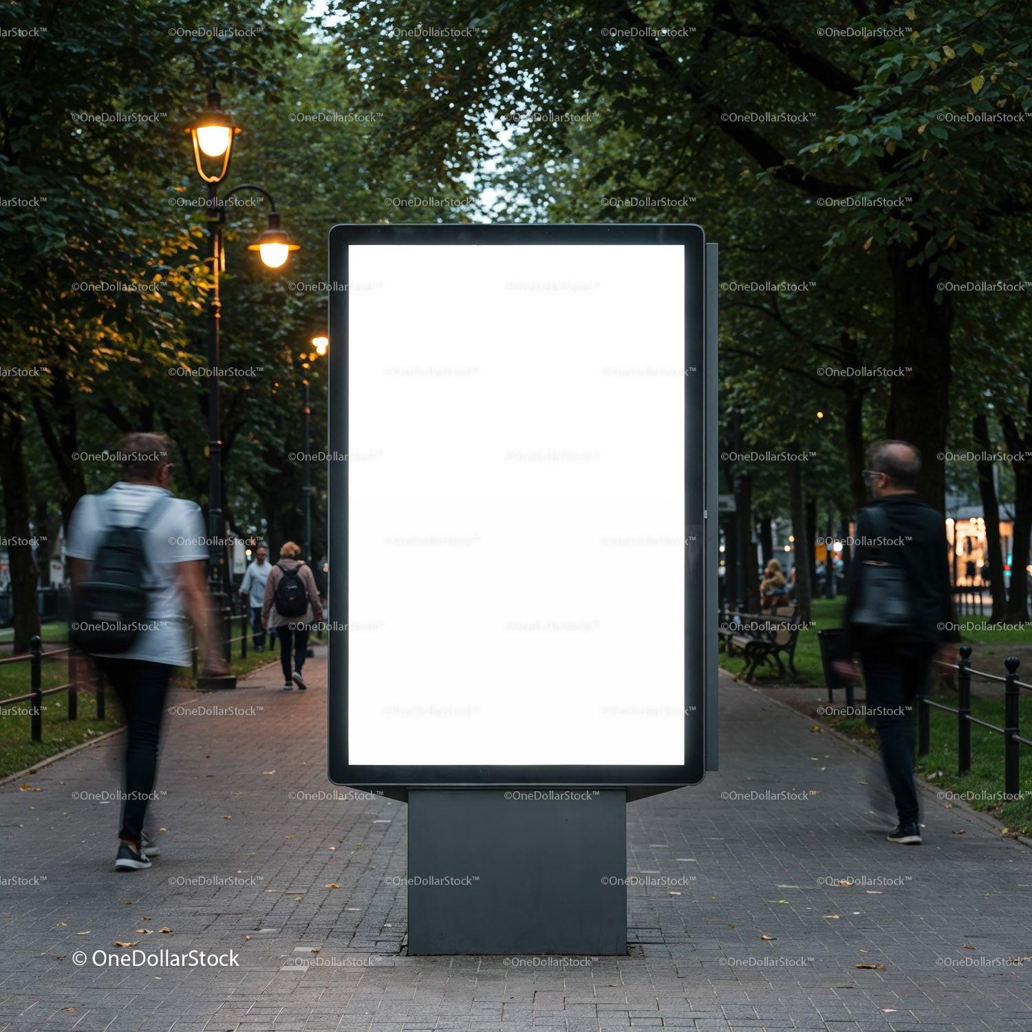 Empty illuminated billboard on city park walkway at dusk
