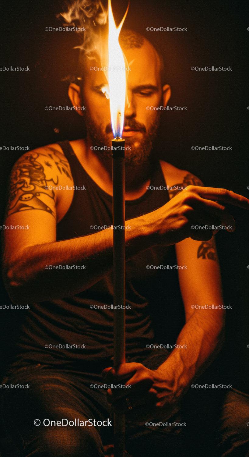 Man with tattoos illuminated by tall candle flame