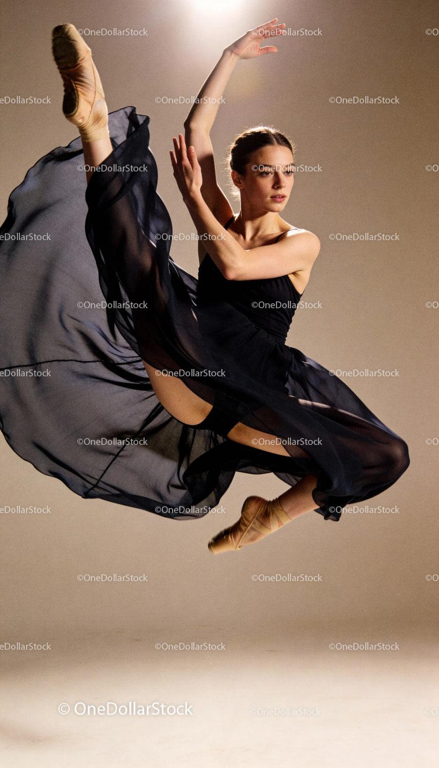 Graceful ballerina performing a high leap in black dress