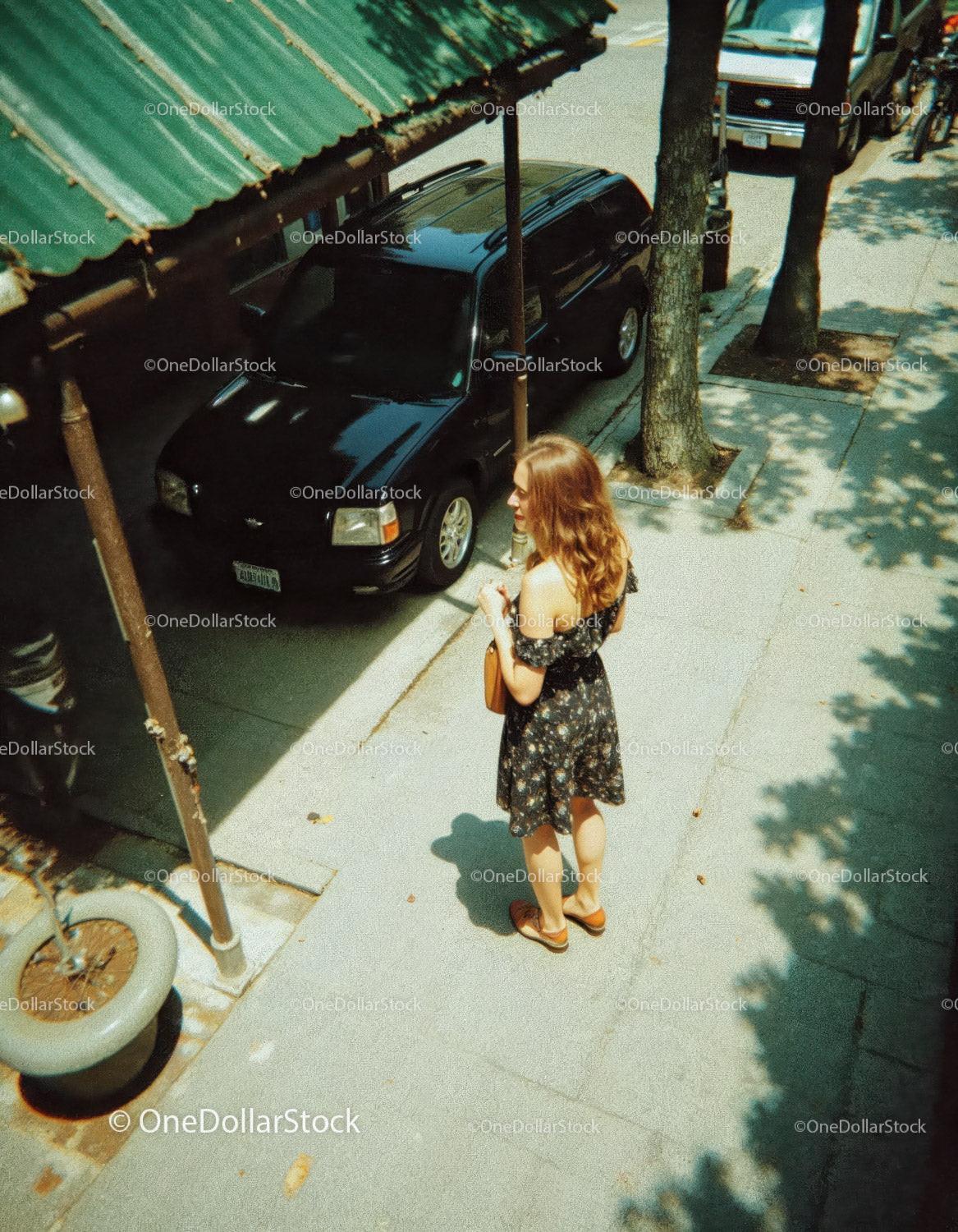 Woman in Floral Dress Standing on Sidewalk Near Parked Car in City