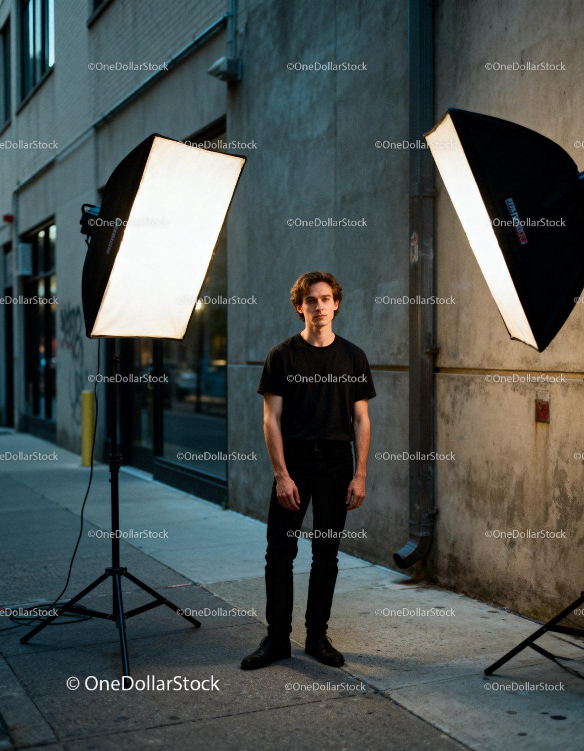 Young man in black outfit illuminated by studio lights outdoors