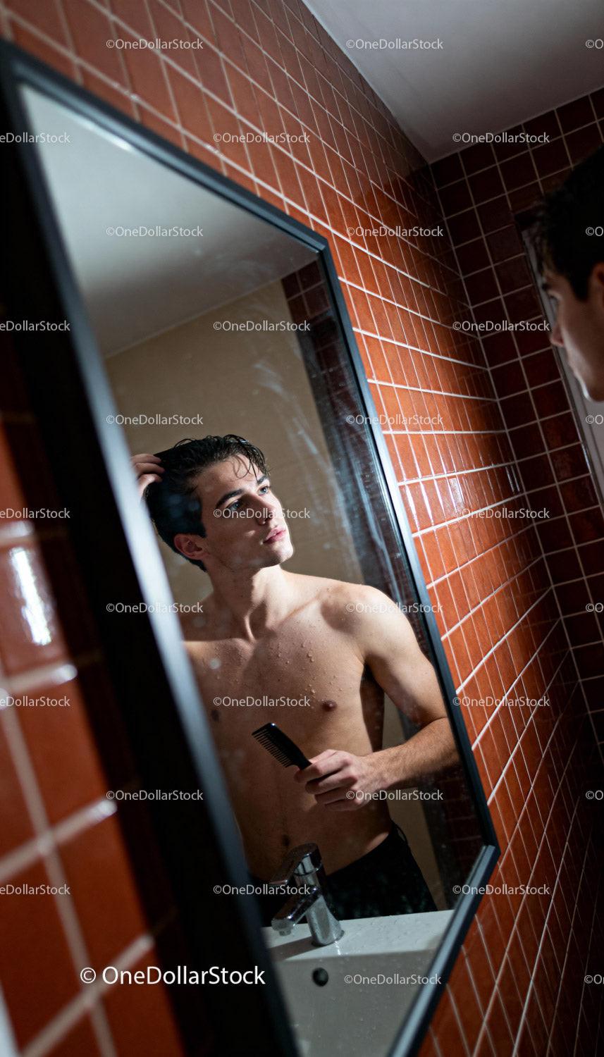Young man grooming hair in bathroom mirror