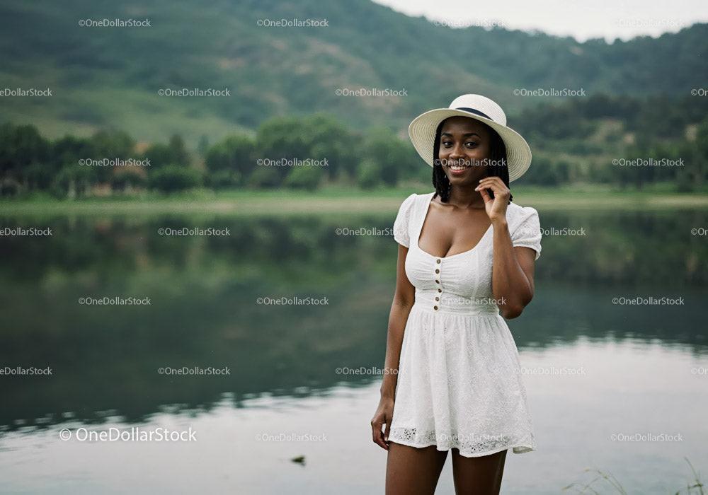 Stylish Woman in White Dress and Hat Enjoys Lake Scene