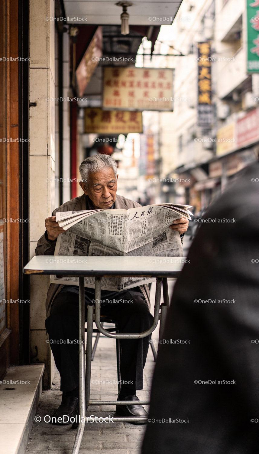 Elderly man reading newspaper in Asian street cafe