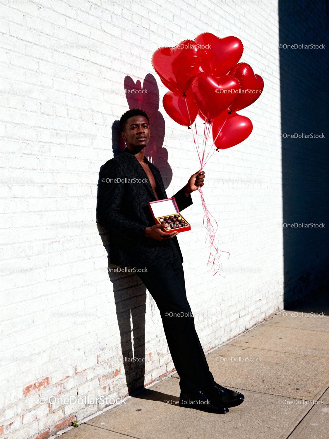Stylish man holding heart balloons and chocolates gift