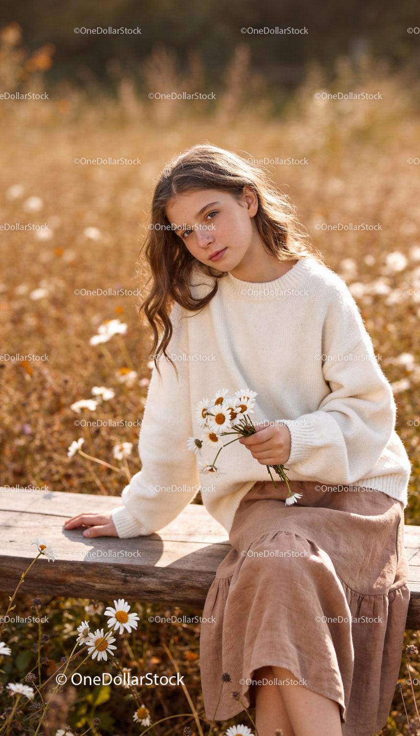 Young woman in white sweater holding daisies outdoors