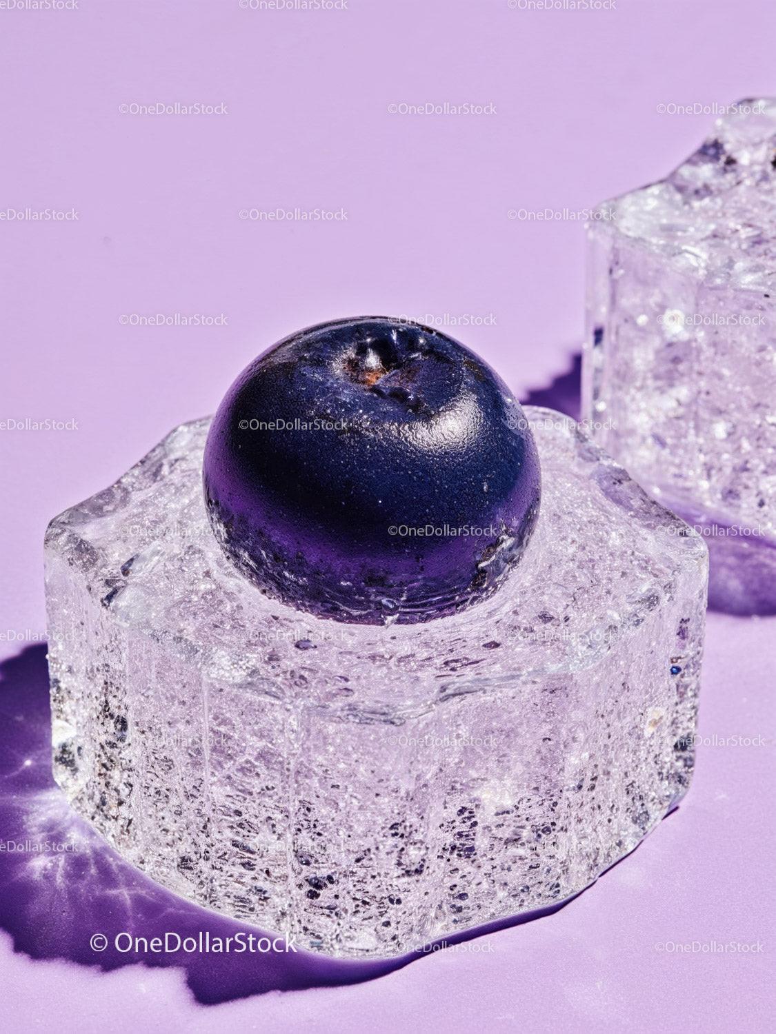 Fresh blueberry resting on clear ice cube on lavender surface
