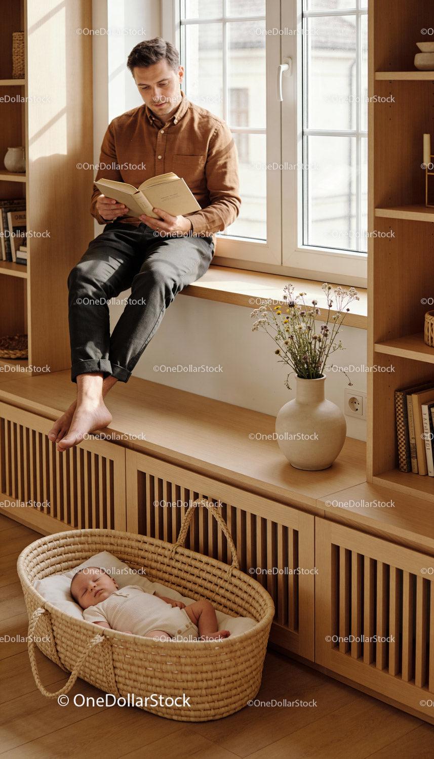 Calm father reading by window while baby sleeps below