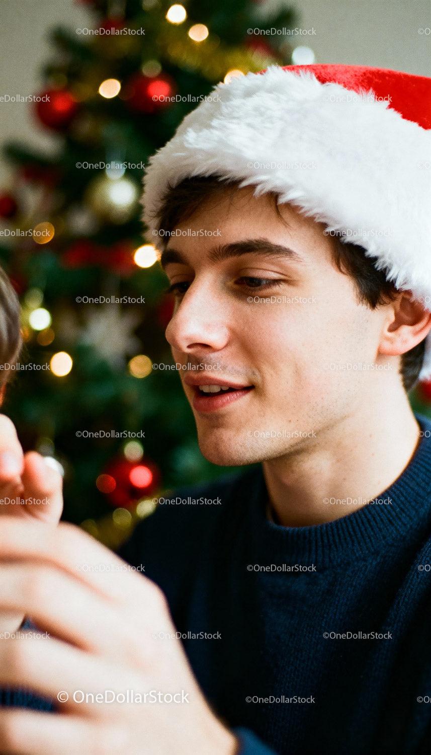 Young man wearing Santa hat decorating Christmas tree