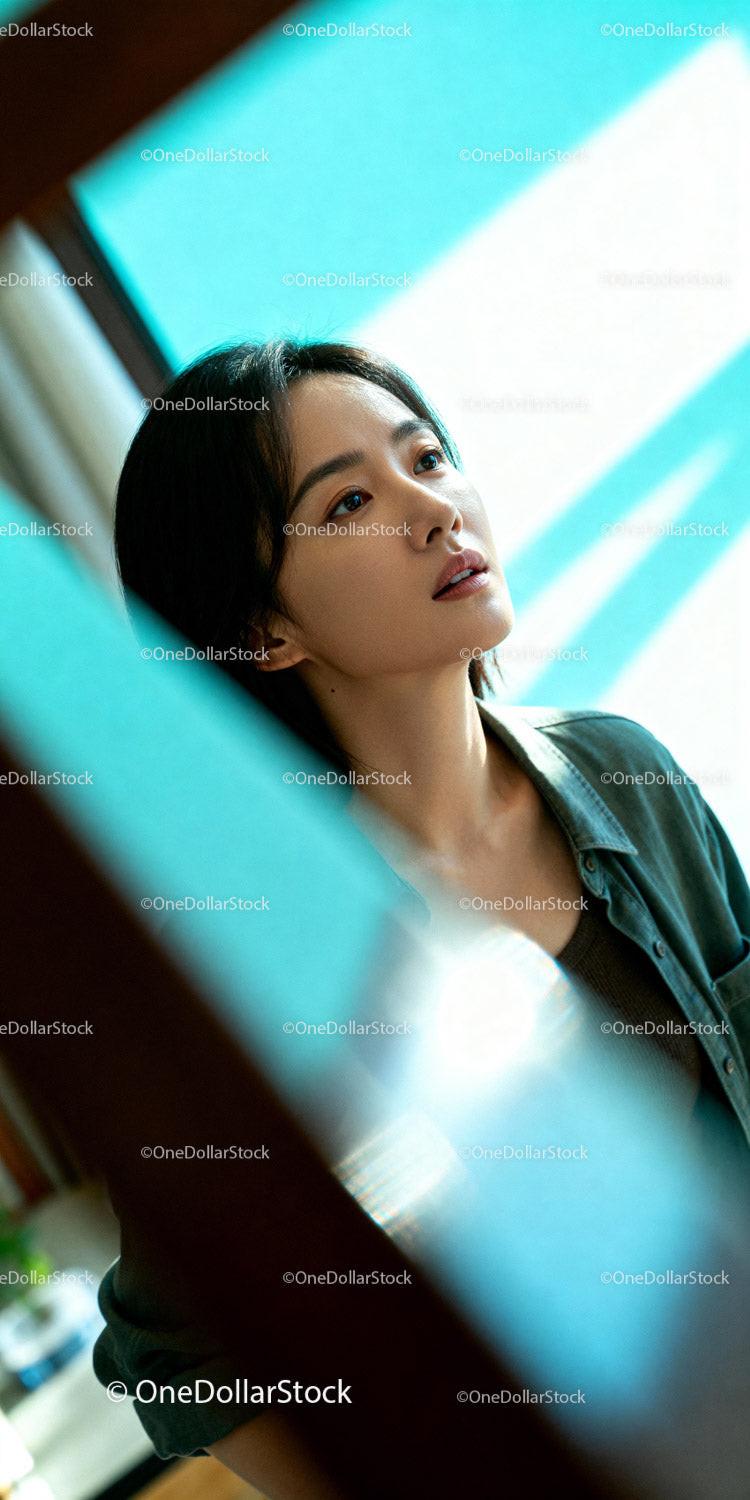 Thoughtful young woman gazing through window light