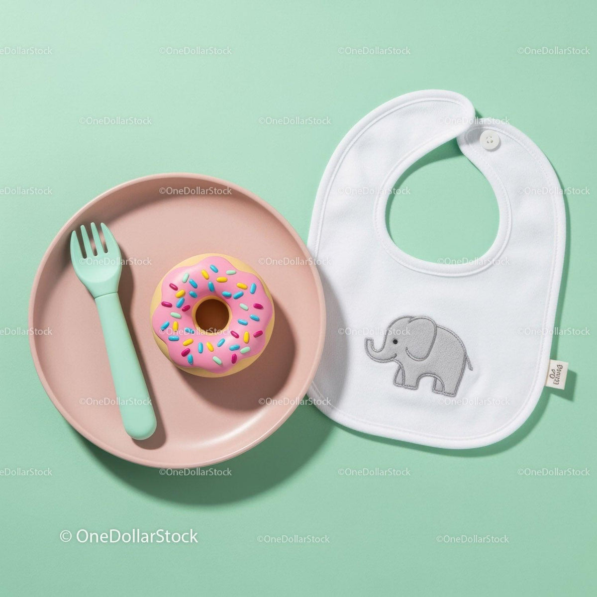 Baby feeding set with toy donut and bib on green table