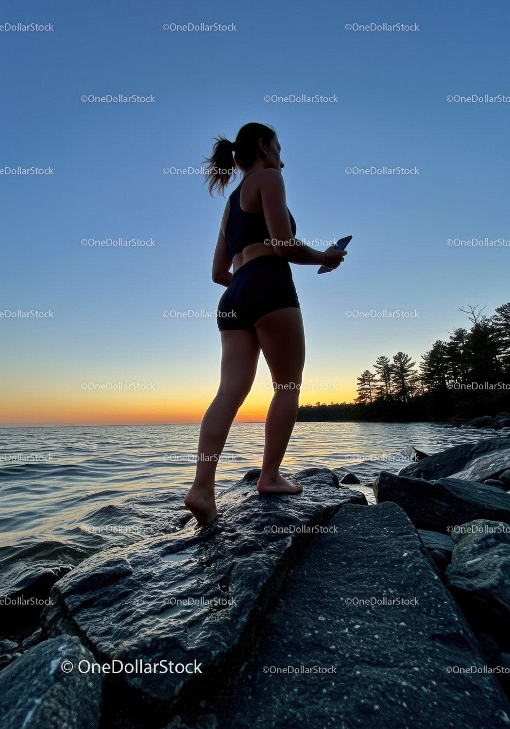 Young woman standing on rocks by lake at sunset