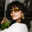 Chic Woman Wearing Yellow Sunglasses and Green Earrings Sipping Green Drink