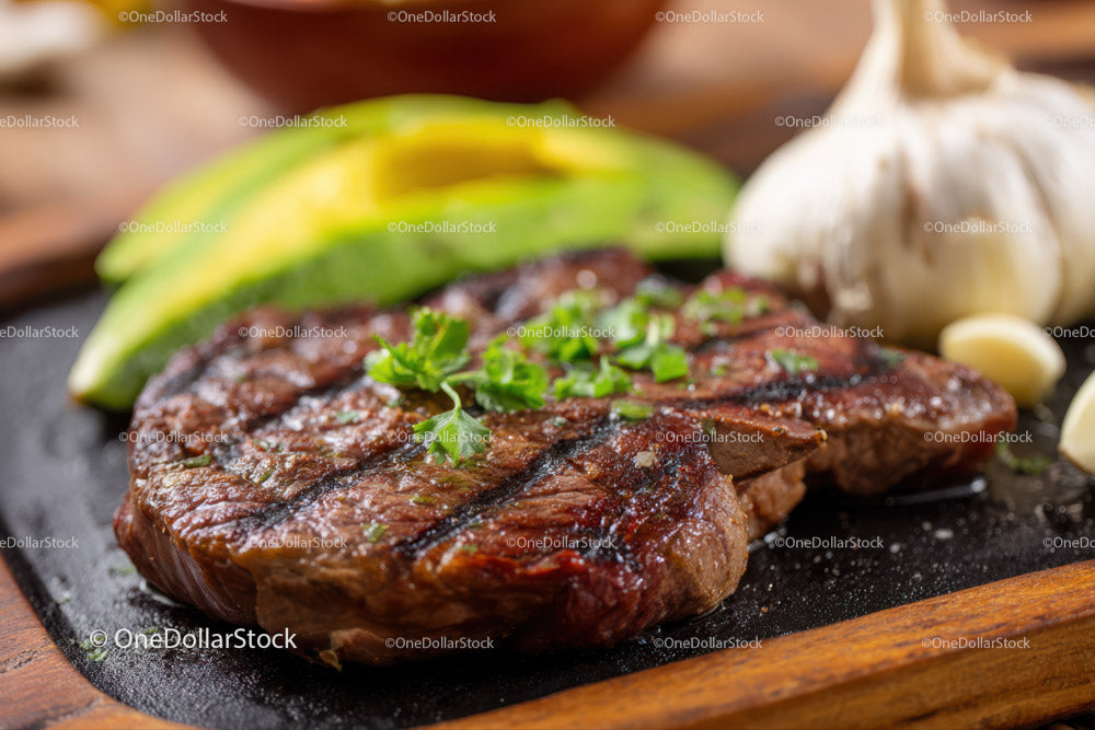 Grilled Steak with Avocado and Garlic Cloves on a Wooden Platter