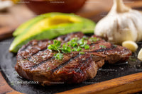 Grilled Steak with Avocado and Garlic Cloves on a Wooden Platter