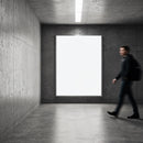 Person walking past illuminated blank poster in modern hall