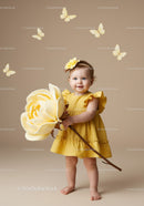 Smiling toddler girl holding huge yellow flower indoors