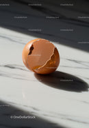 Cracked brown eggshell casting shadow on marble surface